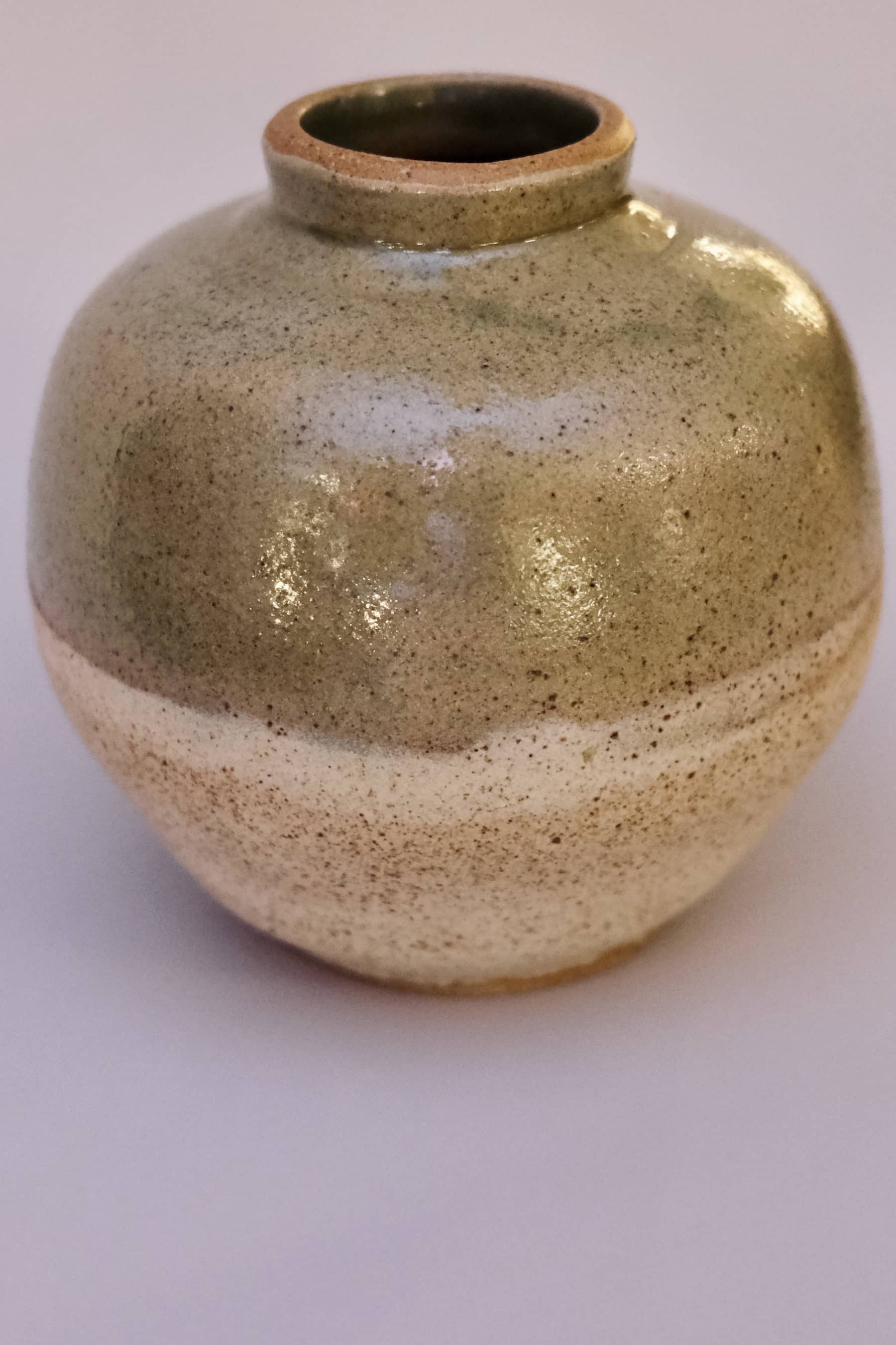 Small spherical bud vase with sage green and cream glaze and heavy iron speckling.
