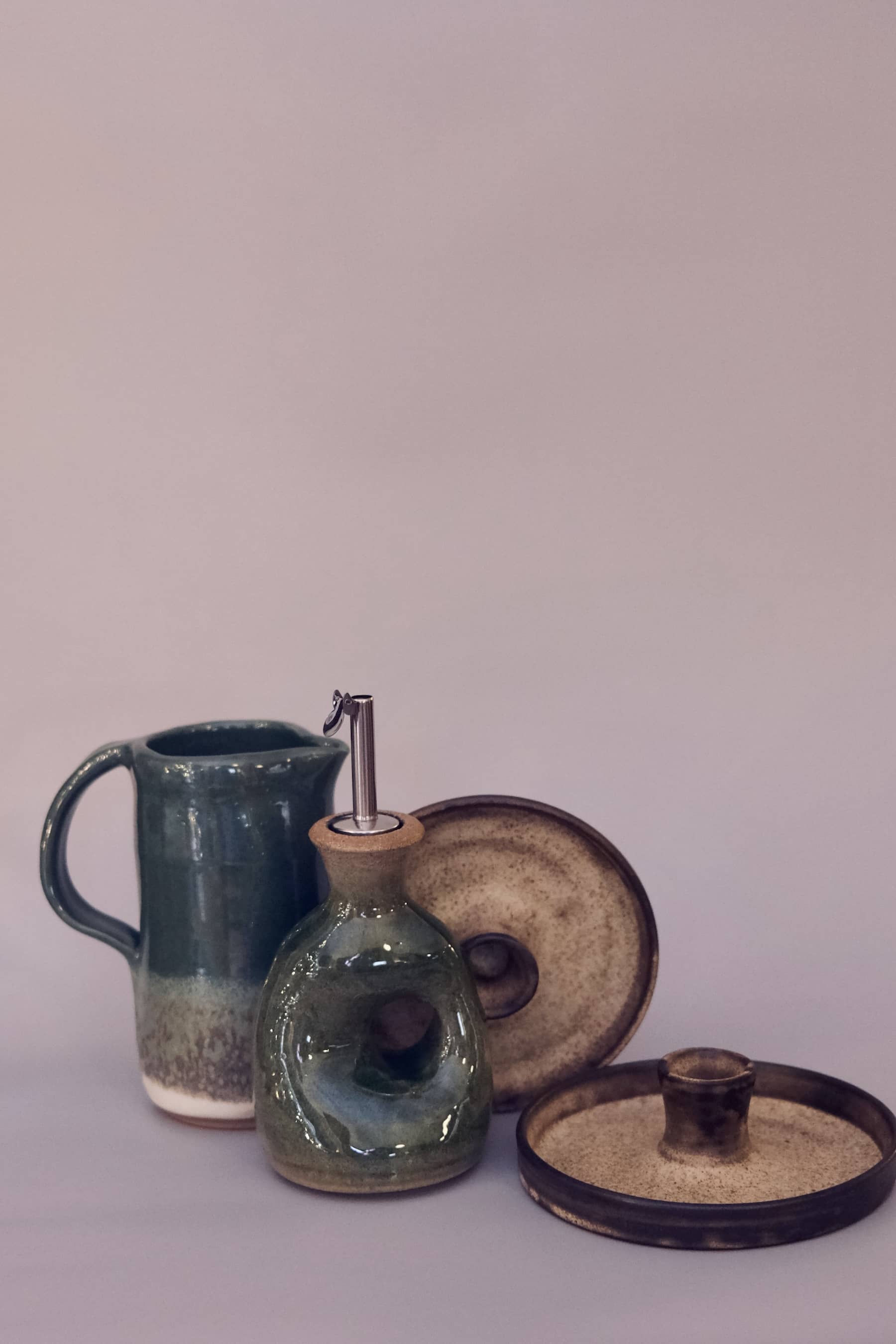 Forest green kitchenware set including a sculptural oil cruet with metal spout, pitcher, and candle holder.