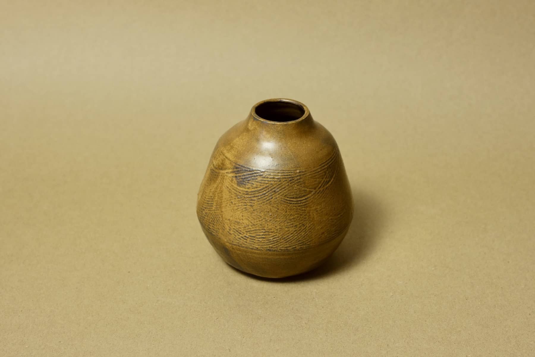 Squat bud vase in toasted ochre clay featuring hand-etched horizontal wave patterns and a narrow rim.