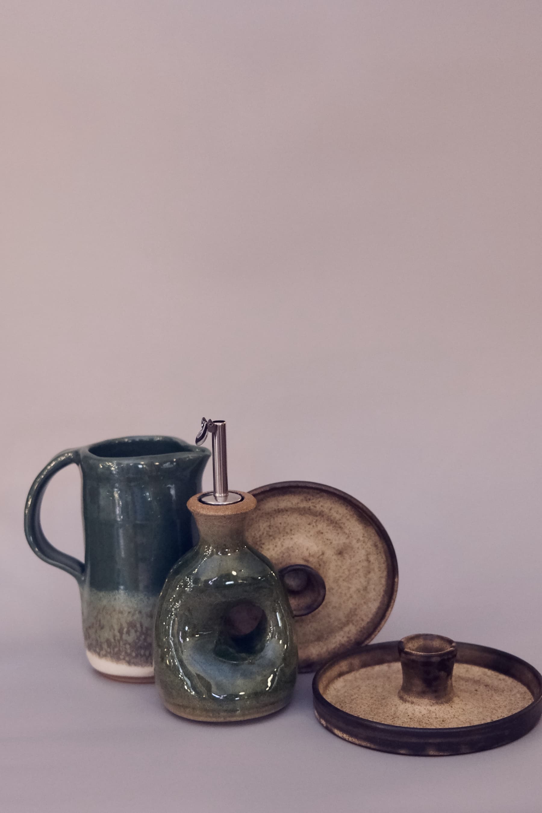 Forest green kitchenware set including a sculptural oil cruet with metal spout, pitcher, and candle holder.