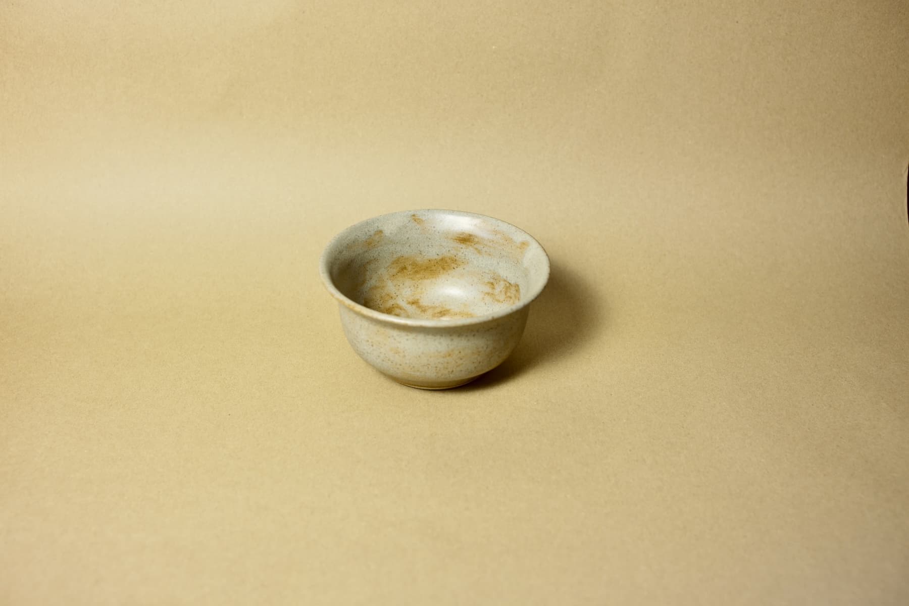 Deep ceramic breakfast bowl in a speckled sand-tone glaze with natural iron spotting and flared rim.