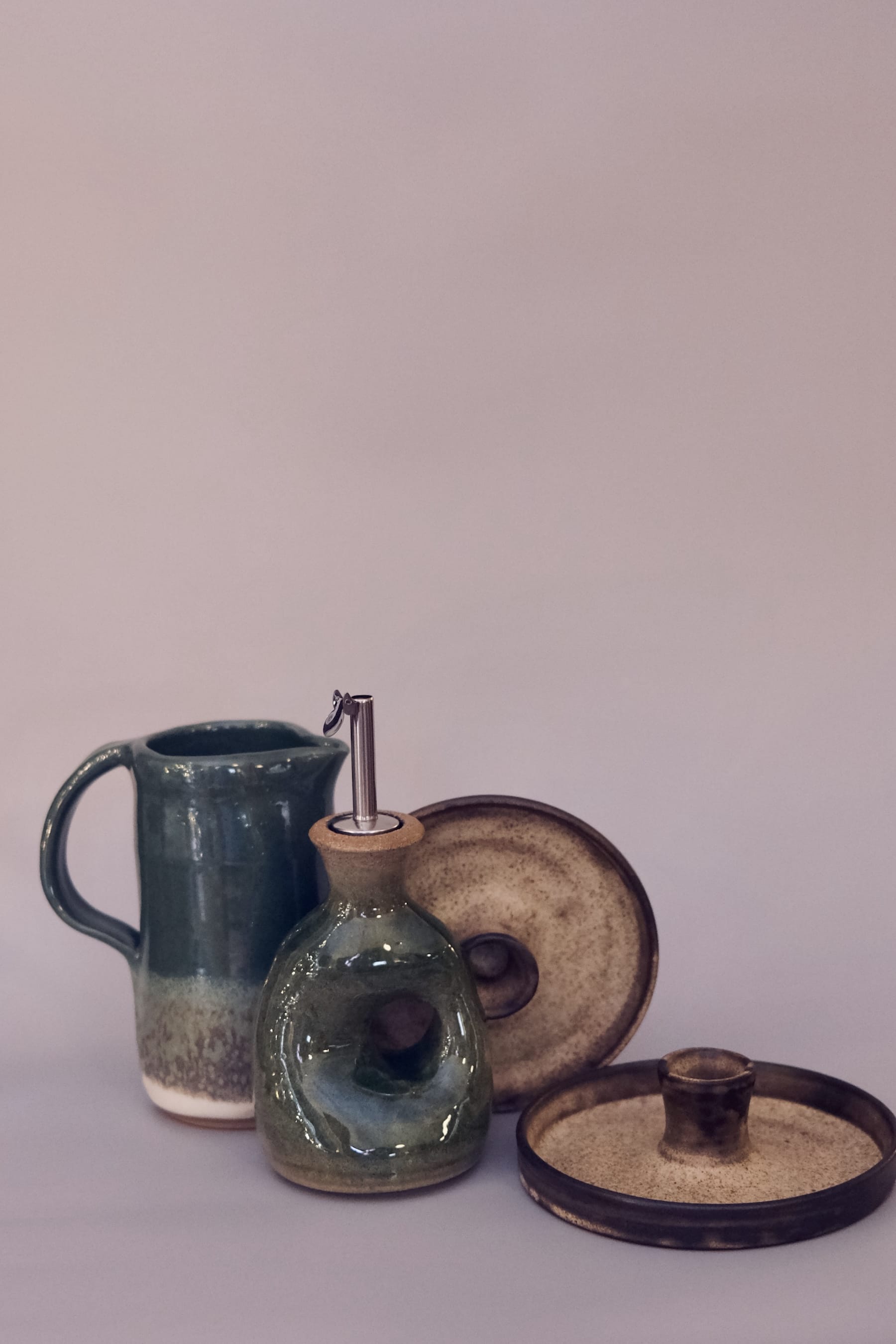 Forest green kitchenware set including a sculptural oil cruet with metal spout, pitcher, and candle holder.